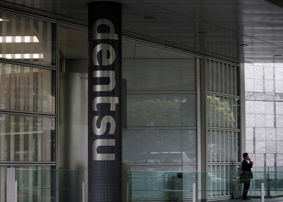 FILE PHOTO: A man speaks on his mobile phone near a logo of Dentsu Co. at the entrance of the company headquarters in Tokyo